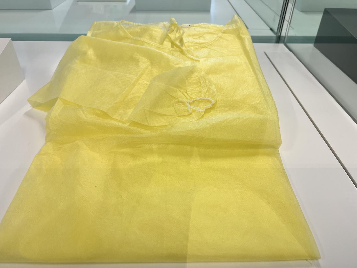 A folded up lemon yellow disposable medical gown made from a thin synthetic material.