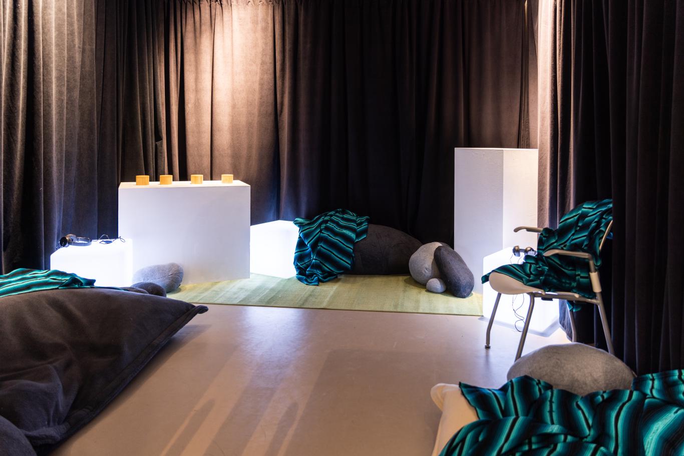 A dimly lit room with pillows and blankets around the edges and interactive elements along the back wall.