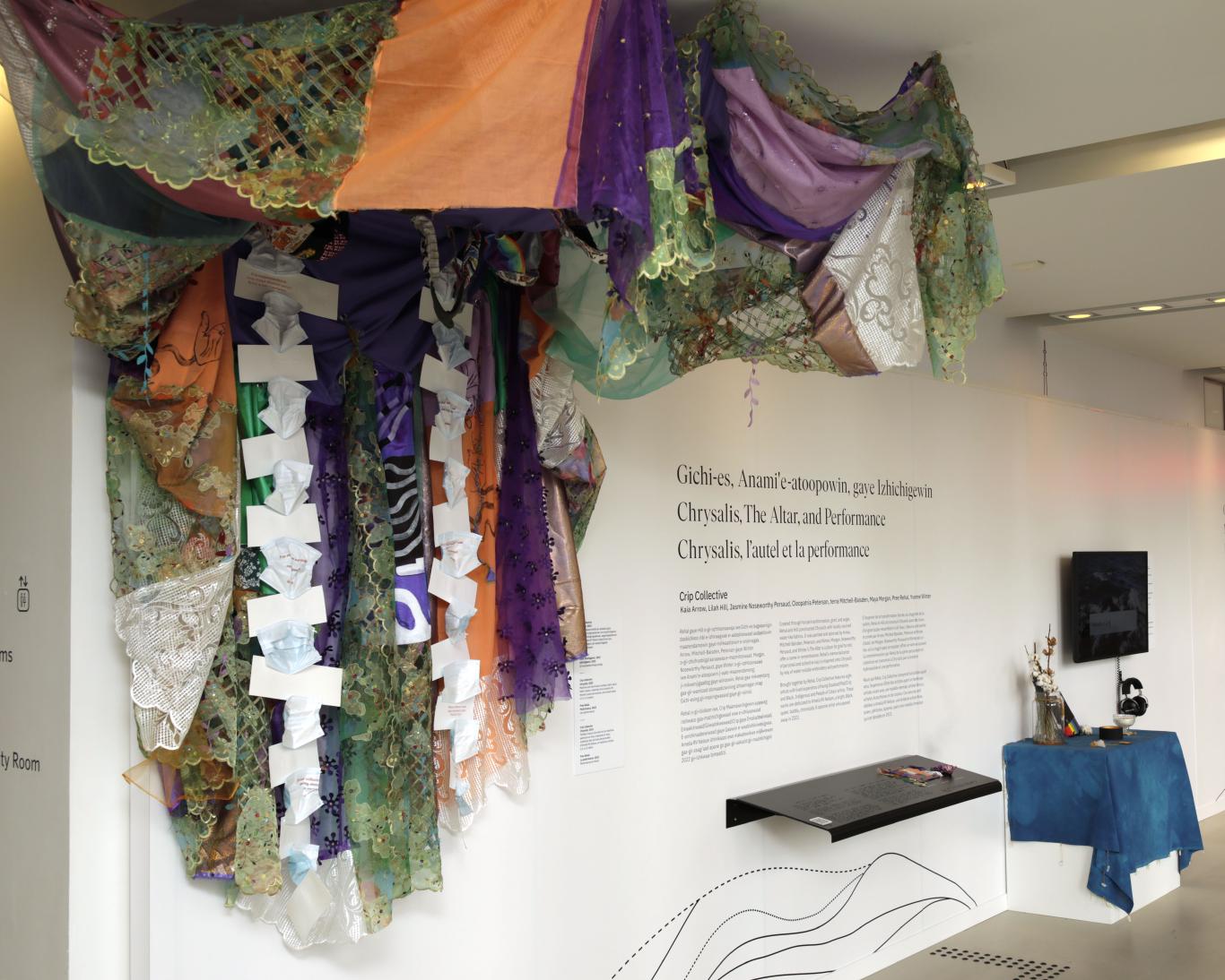 A brightly colored fabric sculpture hangs from the ceiling next to an altar and TV screen.