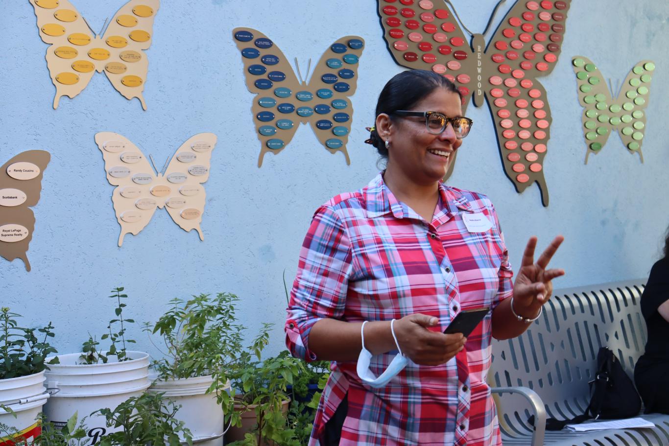 A woman with medium skin tone gestures and smiles in a courtyard