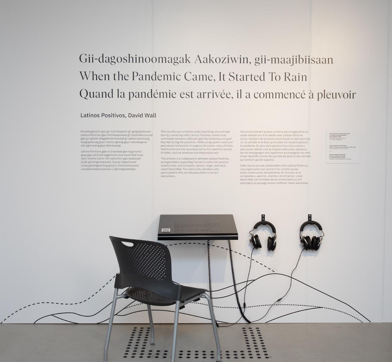 A white gallery wall with large black exhibition text, a reader rail and two sets of headphones.