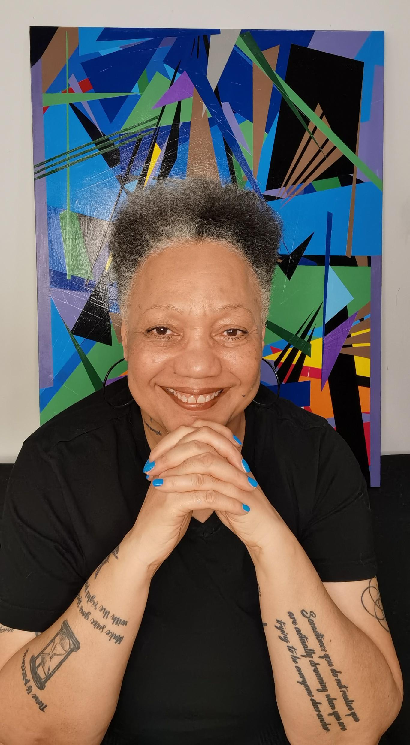 A portrait of a senior woman with medium light skin tone and a short mixed-gray afro, smiling widely at us.